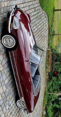 an old red car parked on the side of a brick wall next to a garden