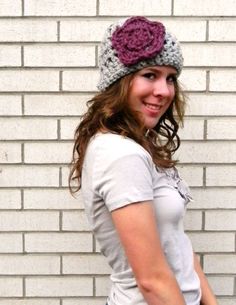 a woman standing in front of a brick wall wearing a crocheted hat with flowers on it