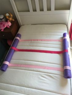 a bed with pink and purple straps on top of it next to a stuffed animal