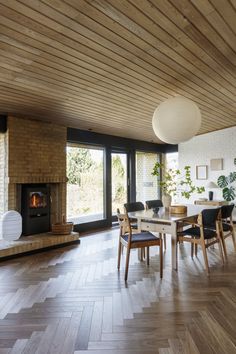 a dining room with wood floors and a fireplace in the center, surrounded by large windows