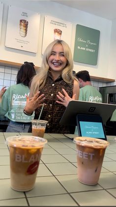 a woman sitting at a table with two cups of coffee in front of her smiling