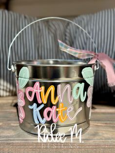 a metal bucket with the words banana kate painted on it and a pink ribbon tied around it