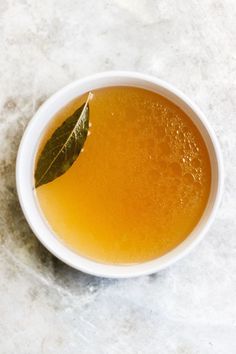 a white bowl filled with liquid and a green leaf