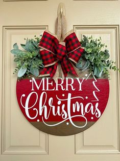 a merry christmas sign hanging on the front door with greenery and ribbon around it