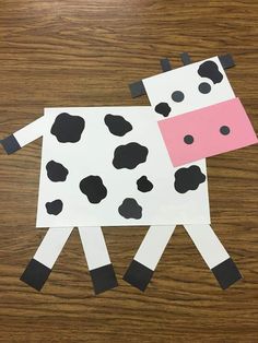 a cow made out of paper sitting on top of a wooden table with black and white spots