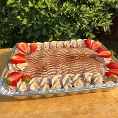 there is a cake with strawberries on it sitting on a wooden table in front of some bushes