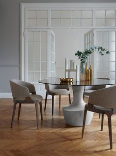 a glass table with chairs around it in front of a white wall and wooden floor