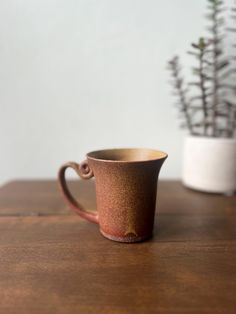 a brown cup sitting on top of a wooden table next to a potted plant