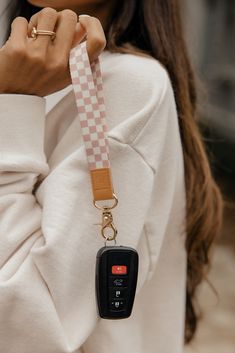 a woman wearing a white sweater holding a pink and white checkered keychain