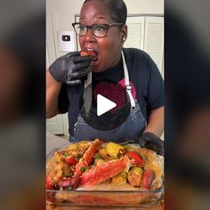 a woman in an apron eating food from a casserole dish with lobsters and corn on the cob