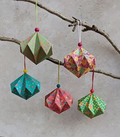 four colorful origami ornaments hanging from a tree branch with no leaves on it