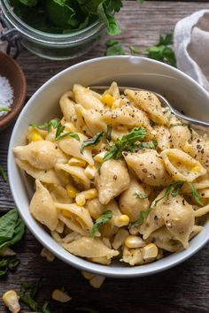 a white bowl filled with pasta and garnished with herbs on top of a wooden table