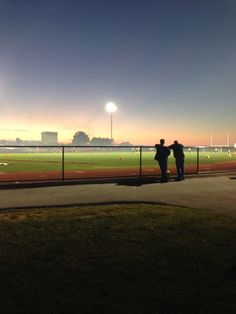 two people standing next to each other near a fence on a baseball field at night