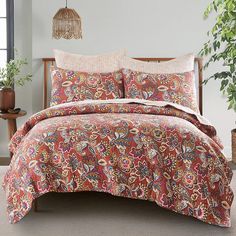 a bed covered in a red paisley comforter next to a potted plant