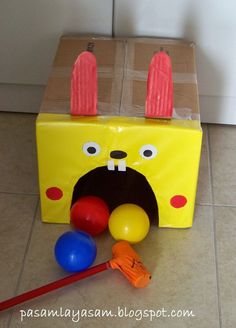 a yellow box with red ears and two balls in front of it on the floor