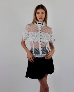 Introducing the elegant Alicia Blouse, crafted from Swiss Point D’Esprit with cotton lace ruffles, Venise trims, and satin baby bows. This soft, fitted blouse features an empire focus, adorned with delicate ruffles at the neckline and sleeves, complemented by satin pearl buttons at the center front. Available in White and Black or Black on Black. Swiss Point D’Esprit Cotton lace ruffles with Venise trims Satin pearl buttons Dry clean only Each piece is made to order and handcrafted in our atelie Luxury Blouse With Lace Trim, Elegant Spring Lace Top With Contrast Lace, Elegant Spring Tops With Contrast Lace, Elegant Tops With Contrast Lace For Spring, Short Sleeve Lace Top With Ruffles, White Elegant Tops With Contrast Lace, Elegant White Tops With Contrast Lace, Chic Short Sleeve Blouse With Lace Patchwork, Short Sleeve Lace Tops With Ruffles