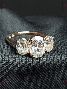 three stone diamond ring sitting on top of a black piece of cloth in front of the camera