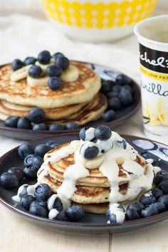 pancakes with blueberries and whipped cream are on black plates next to a cup of coffee