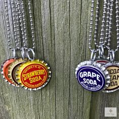 three soda bottle caps are hanging on a wooden fence with chain necklaces attached to them