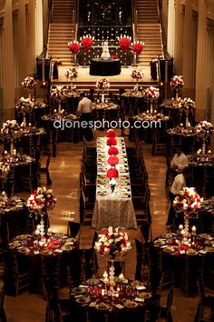 a banquet hall filled with lots of tables covered in red and white flowers, candles and centerpieces