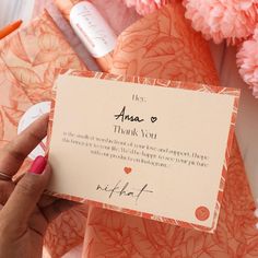 a person holding up a thank card in front of some pink flowers and other items