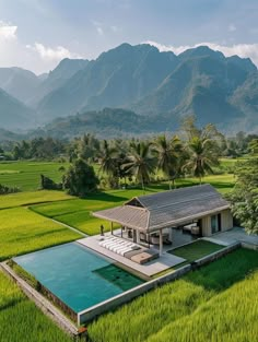 an aerial view of a house in the middle of rice fields with mountains in the background