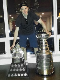 a man standing next to two trophies in front of a window