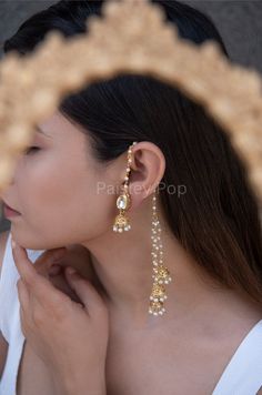 The gold-plated kundan jhumkis are traditionally inspired by the rich Indian Heritage of jewelry making. The design of the bridal jhumkis earrings features pearl hangings and a top encrusted with kundan. These ethnic jhumkis have a gold-plated pearl chain that gives them a delicate and elegant look. The richly traditional design is versatile and can be paired with almost anything Indian.  Closure - Push Back Handcrafted in Jammu and Kashmir  Paisley Pop travels the depths of India to learn techniques and crafts from deep down the local markets and villages. We give utmost importance to our quality and packaging. Our goal is to make sure you receive exactly what you are looking for and for your experience to be a special and memorable one. We are ready to help and advise you through your pu Gold Jewellery Bridal Indian, Simple Indian Earrings, Jhumka Designs Gold Indian, Earrings With Chain Indian, Traditional Earrings Indian Jewelry, Indian Pearl Earrings, Ethnic Jewelry Indian, Indian Bridal Earrings, Big Jhumka Earrings