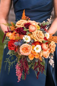 a woman in a blue dress holding a bouquet of orange and red flowers on her wedding day