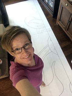 a woman in glasses is cutting out a paper pattern on the floor with scissors and tape