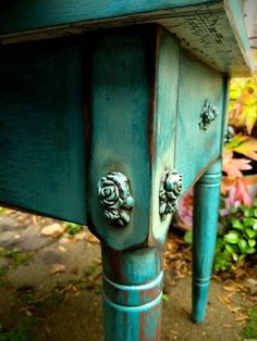 an old blue painted table with flowers on the top and bottom, sitting in front of some bushes