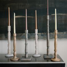 a group of candles sitting on top of a wooden table next to a wall with a painting behind it