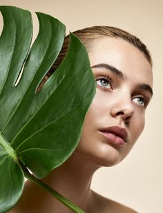 a woman holding a large green leaf in front of her face