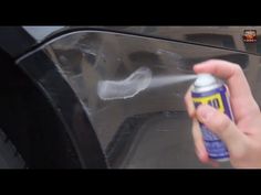 a person is spraying something on the side of a car with a spray bottle in front of it