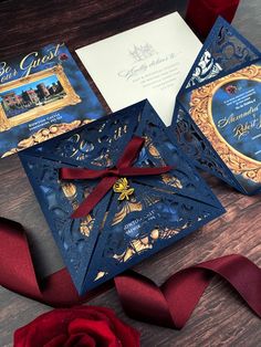 an ornate blue and gold wedding card with a red rose on the table next to it