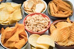 several bowls filled with chips and crackers on top of a white tablecloth,