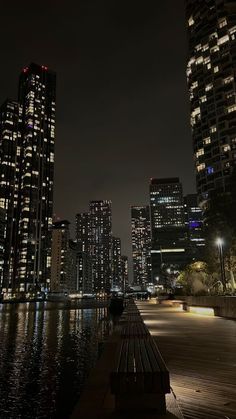 a bench sitting on the side of a river in front of tall buildings at night