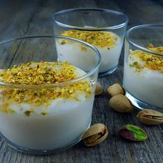 three glasses filled with yogurt and nuts on top of a wooden table next to each other