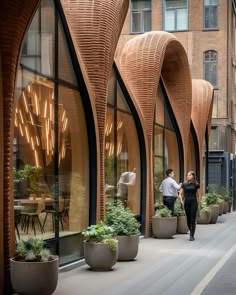 two people walking down the sidewalk in front of an office building with large planters