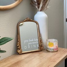 there is a mirror, vase with feathers and a drink glass on the table next to it