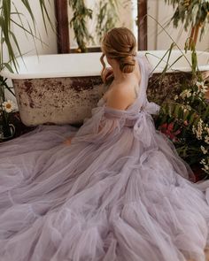 a woman in a purple dress sitting on the floor next to a tub with flowers