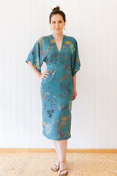 a woman standing in front of a white wall wearing a blue dress with flowers on it