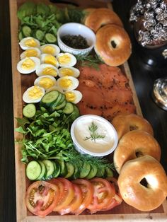 a wooden cutting board topped with bagels and veggies next to other foods