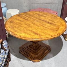 a round wooden table sitting on top of a floor next to two chairs and a couch