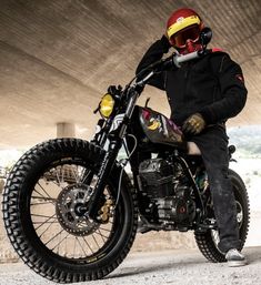 a man sitting on top of a motorcycle under a bridge