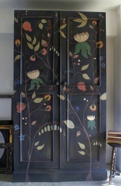 an armoire painted with flowers and leaves on the wall next to a stool in a room