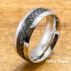 a wedding ring with black carbon fiber inlays on the inside of it, sitting on a wooden surface