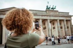 a woman taking a photo with her cell phone in front of the berliner dom