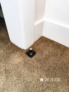 a small black object on the floor next to a white wall and door frame in an otherwise empty room