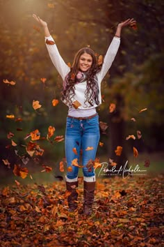 a woman in jeans and boots is throwing leaves into the air with her arms wide open